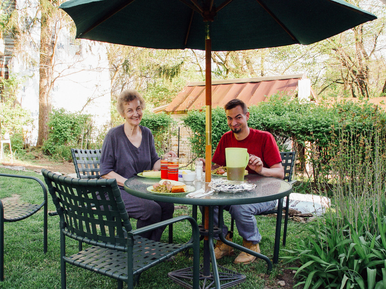 A mother and son sit at a table in a garden