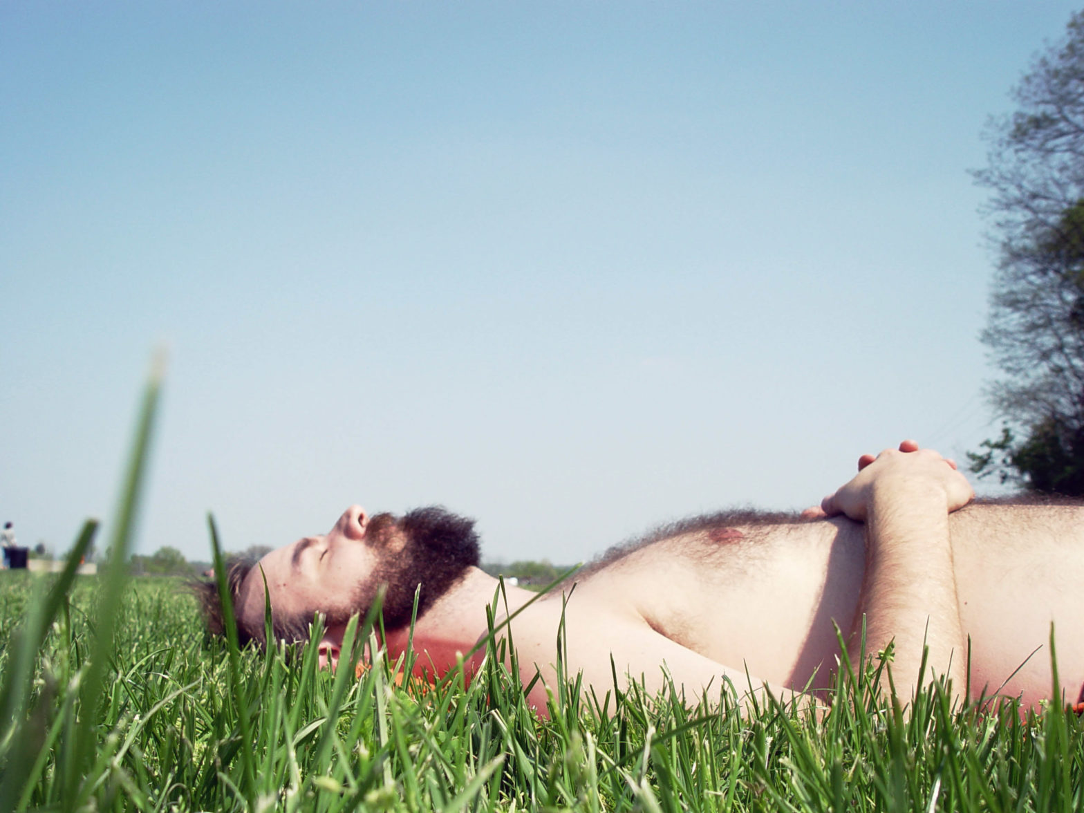 A pale bearded man lies in the grass with his eyes closed