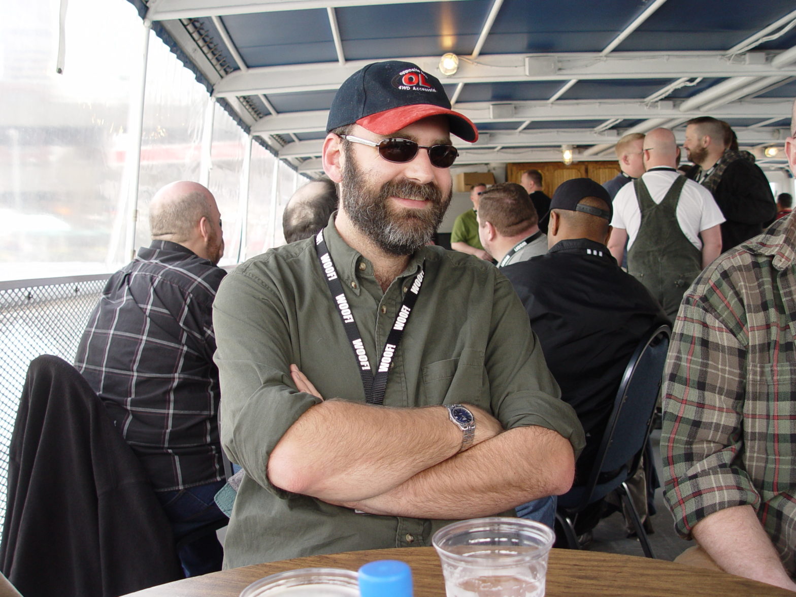 A man with a beard, sunglasses and baseball cap. Arms crossed on a ferry